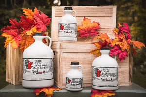 four maple syrup bottles stacked on boxes and surrounded by maple leaves